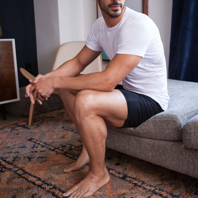 Man sitting on a couch wearing a white undershirt and black sweat proof boxer briefs in a living room.