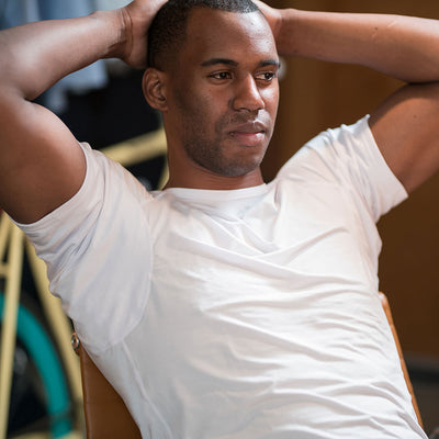 Man in a white Ejis crew neck micro modal sweatproof undershirt, sitting with his hands behind his head, looking relaxed.