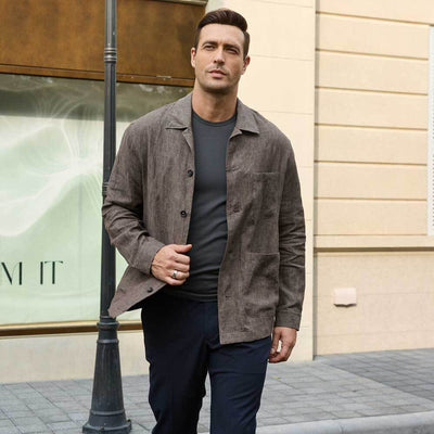 Man wearing a brown jacket over a grey Ejis TotalShield sweat proof t-shirt and dark pants standing on a street.