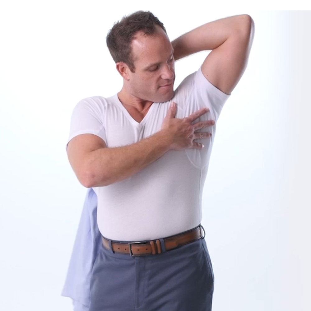 Man in a white Ejis cotton sweat proof undershirt and blue pants touching the underarm pad on his shirt on a white background