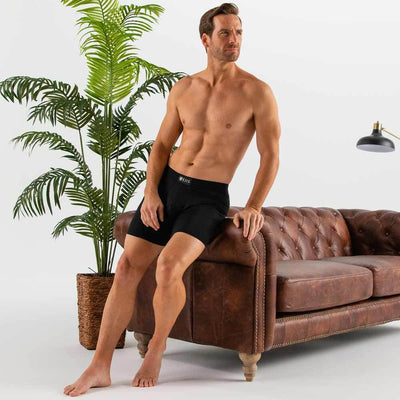 man wearing black Ejis essential boxer briefs leaning against sofa