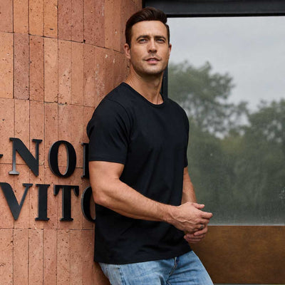 man wearing black TotalShield t-shirt and jeans leaning against brick wall