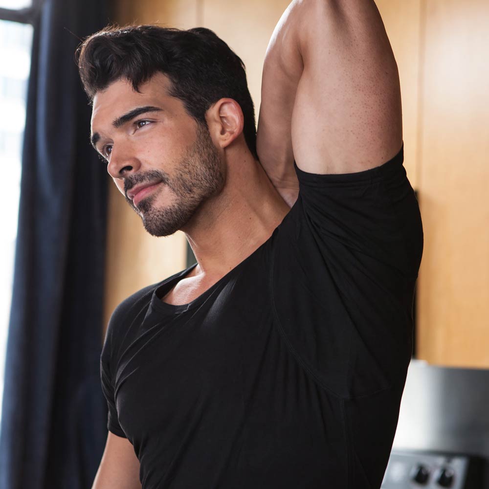 Man in black Ejis v-neck micro modal sweat proof undershirt stretching with a neutral background