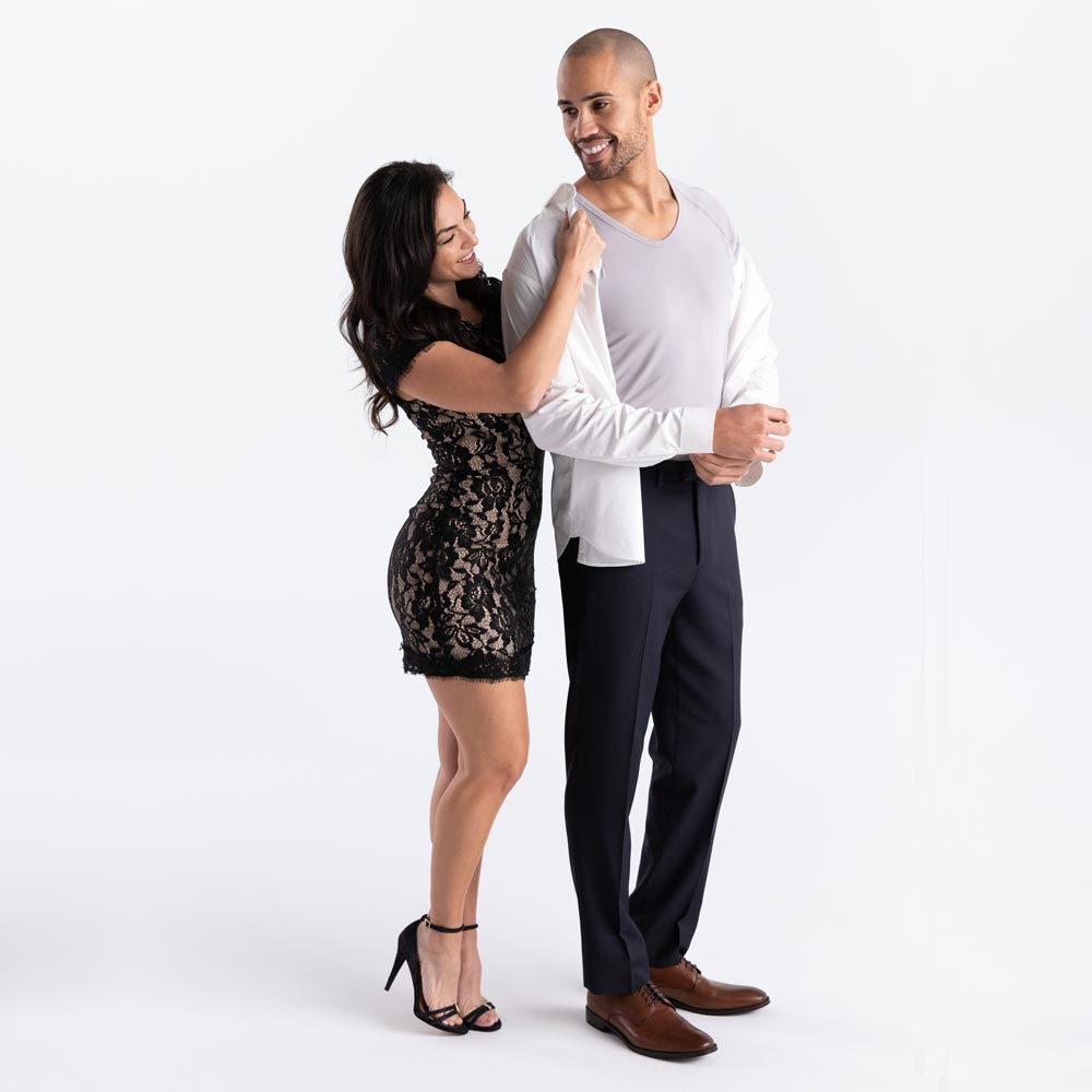 Woman in formal attire helping a man with his dress shirt. He is wearing grey Ejis v-neck micro modal sweat proof undershirt and dress pants  on a white background